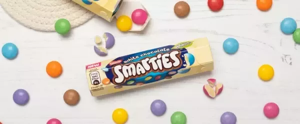 Smarties tube with white colour on the edges and smarties on the table around the tube