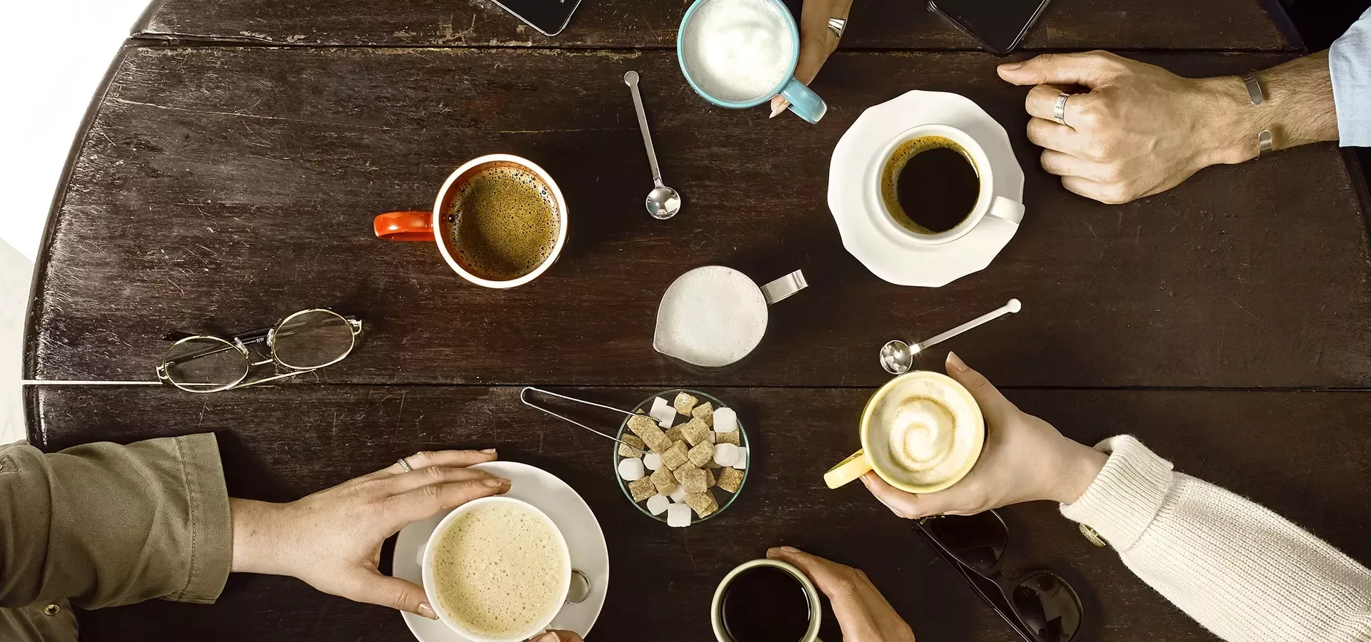 six different types of coffee on a table with people around the table holding the mugs