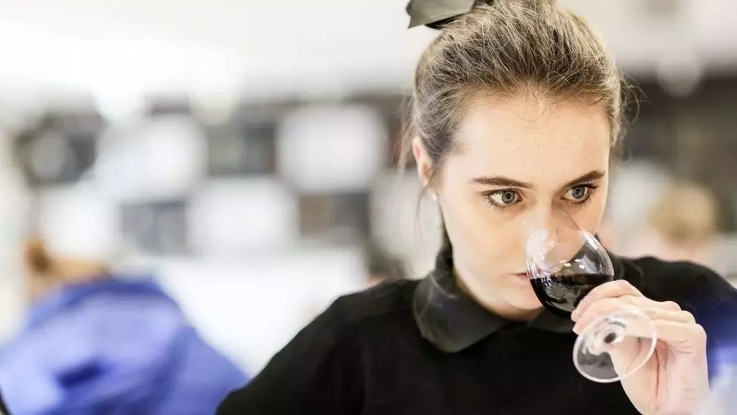 Woman wearing black, with her hair in a bun, smelling a glass of red wine.